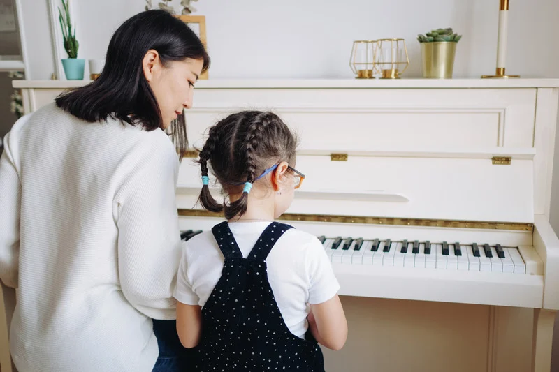 little kid playing piano with mom