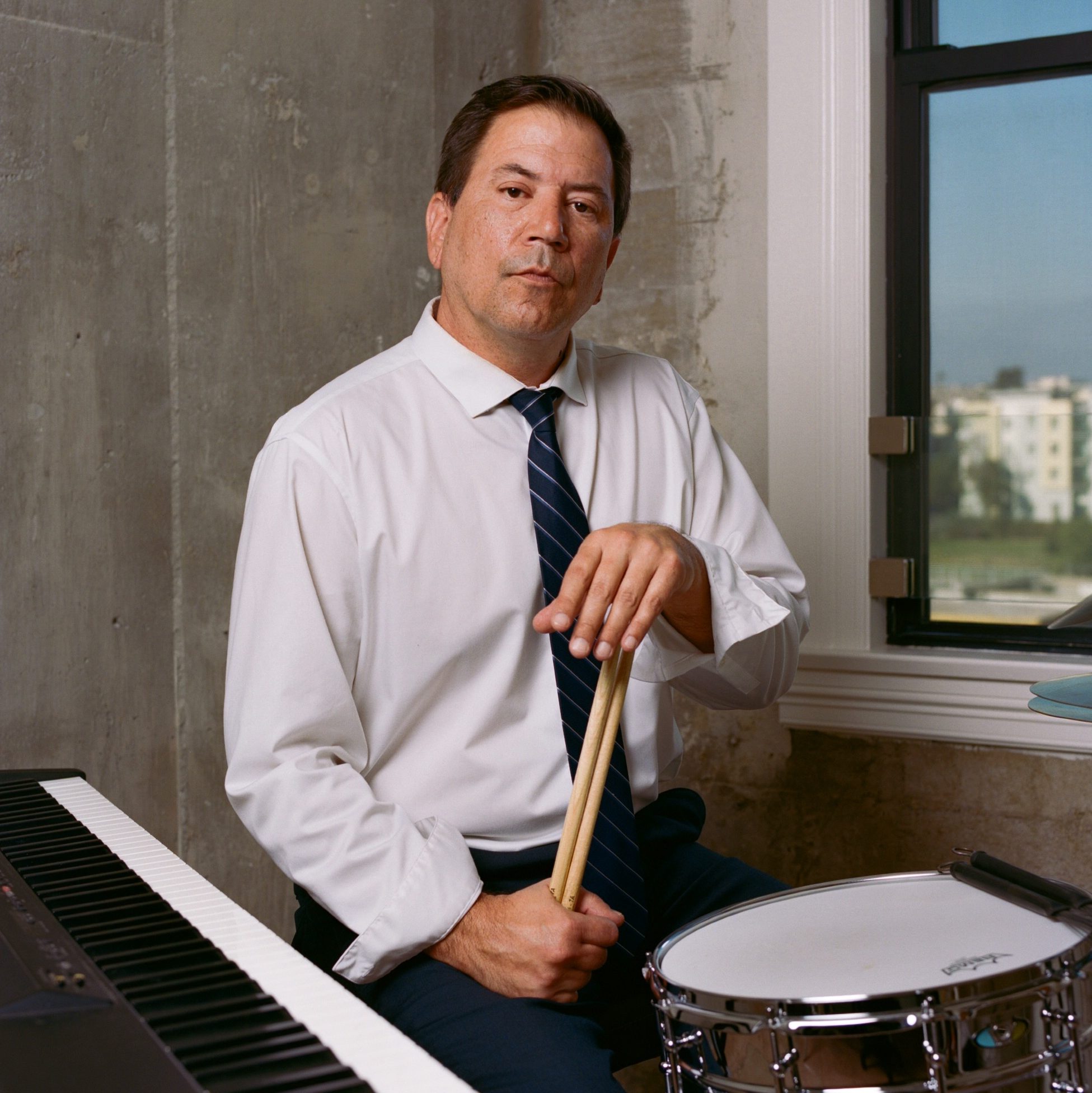 musician holding drumsticks next to a piano and snare drum
